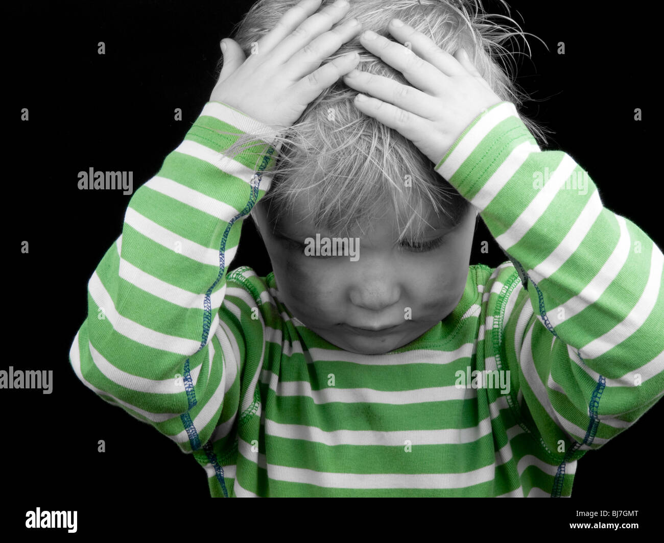 Little boy with hands on his head on black background. Monochrome picture with only color green Stock Photo