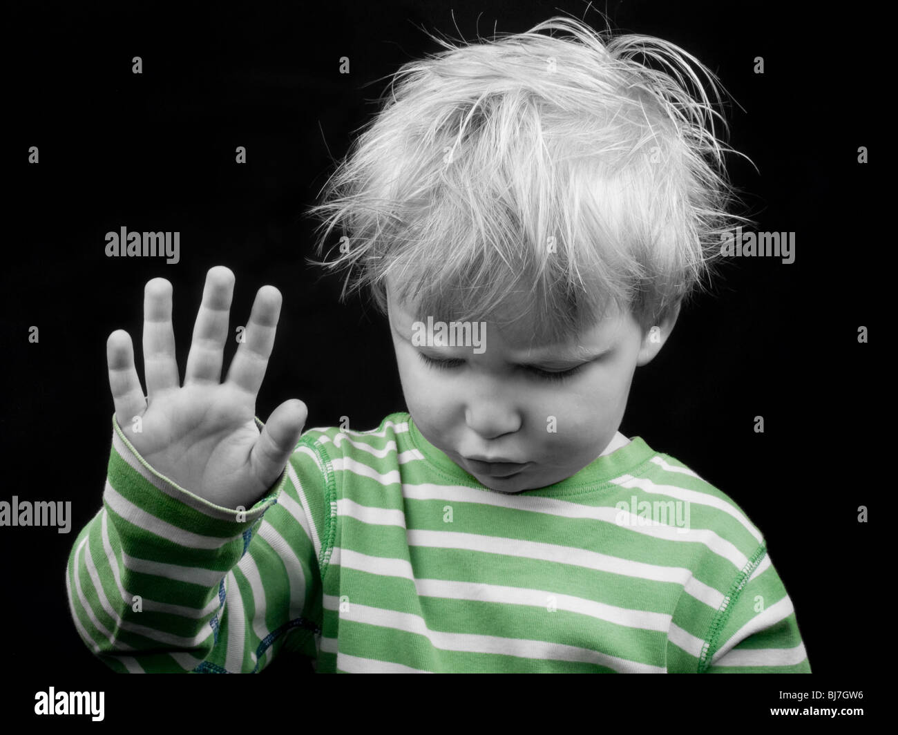 Little boy looking down and showing hand on black background, monochrome picture with only color green Stock Photo