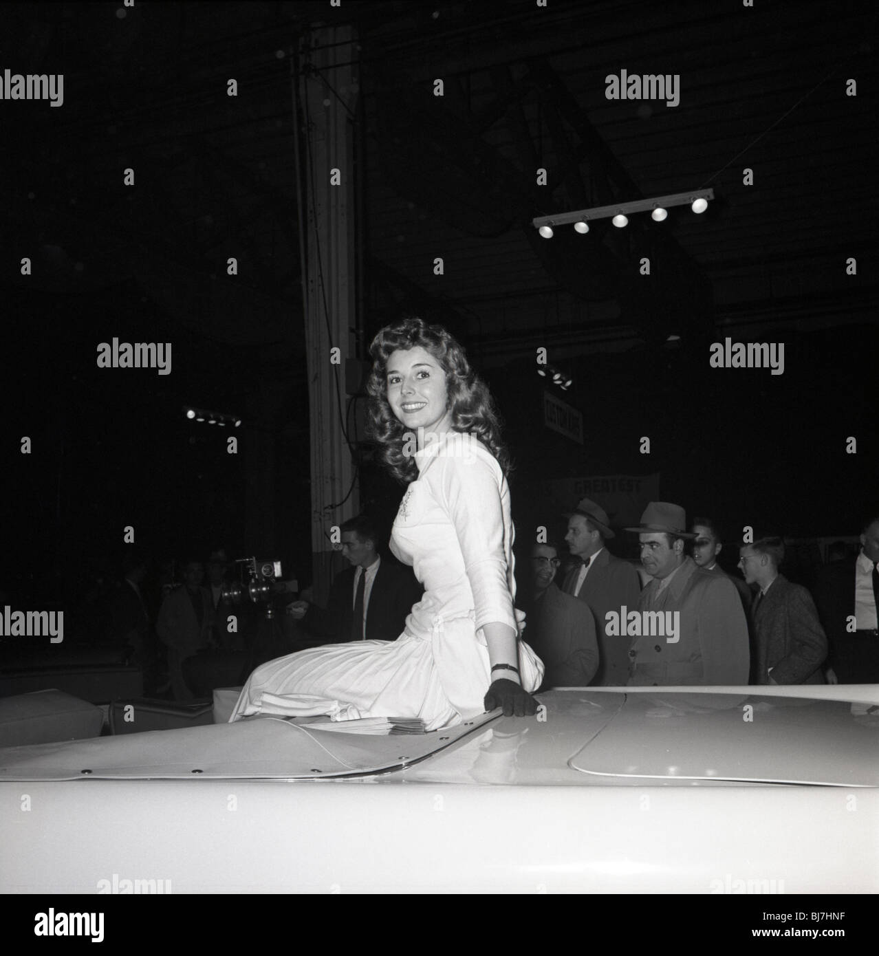 Pretty woman in dress sits on top car during car show in Philadelphia area in the late 1960s. Stock Photo