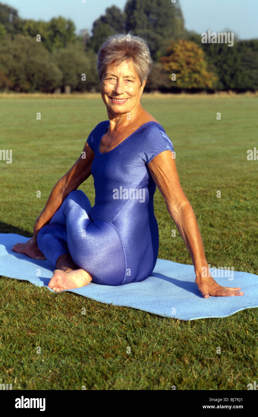 Mature female practising yoga outdoors. Yoga posture. Portrait image of older woman in yoga seated twist. Stock Photo