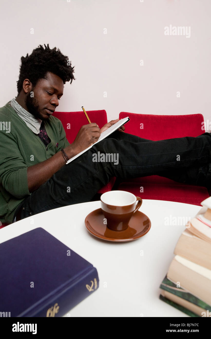 Man writing notes sitting on red sofa Stock Photo - Alamy