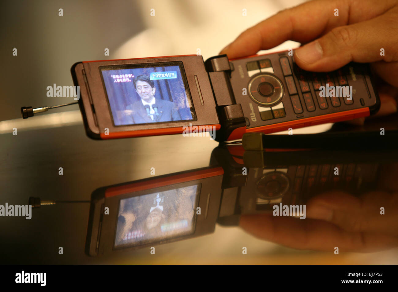 Using a mobile telephone to watch Prime Minister of Japan, Shinzo Abe, on the evening news, Tokyo, Japan Stock Photo
