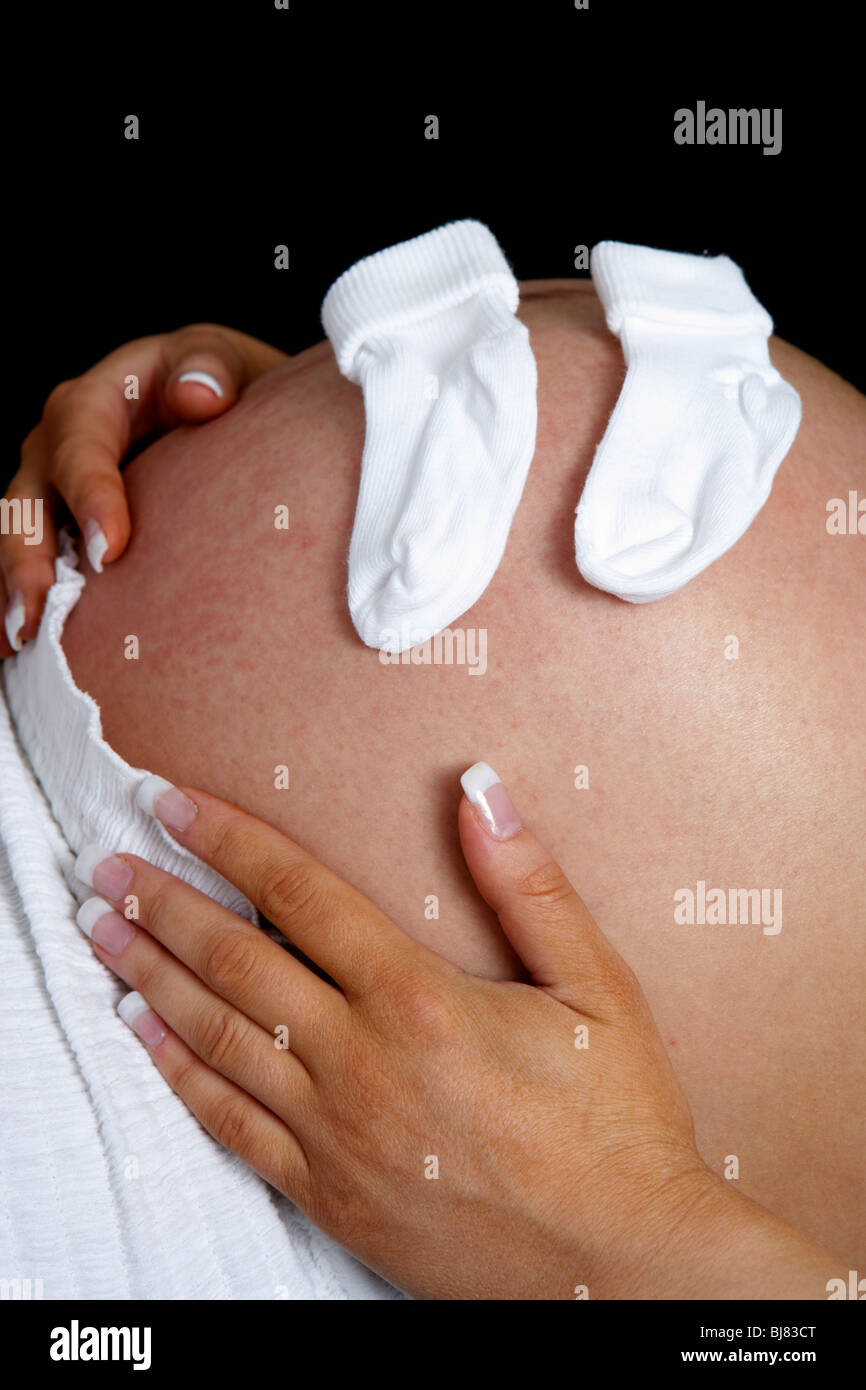 8 month pregnant woman 30 years of age with baby bump and small baby socks Stock Photo
