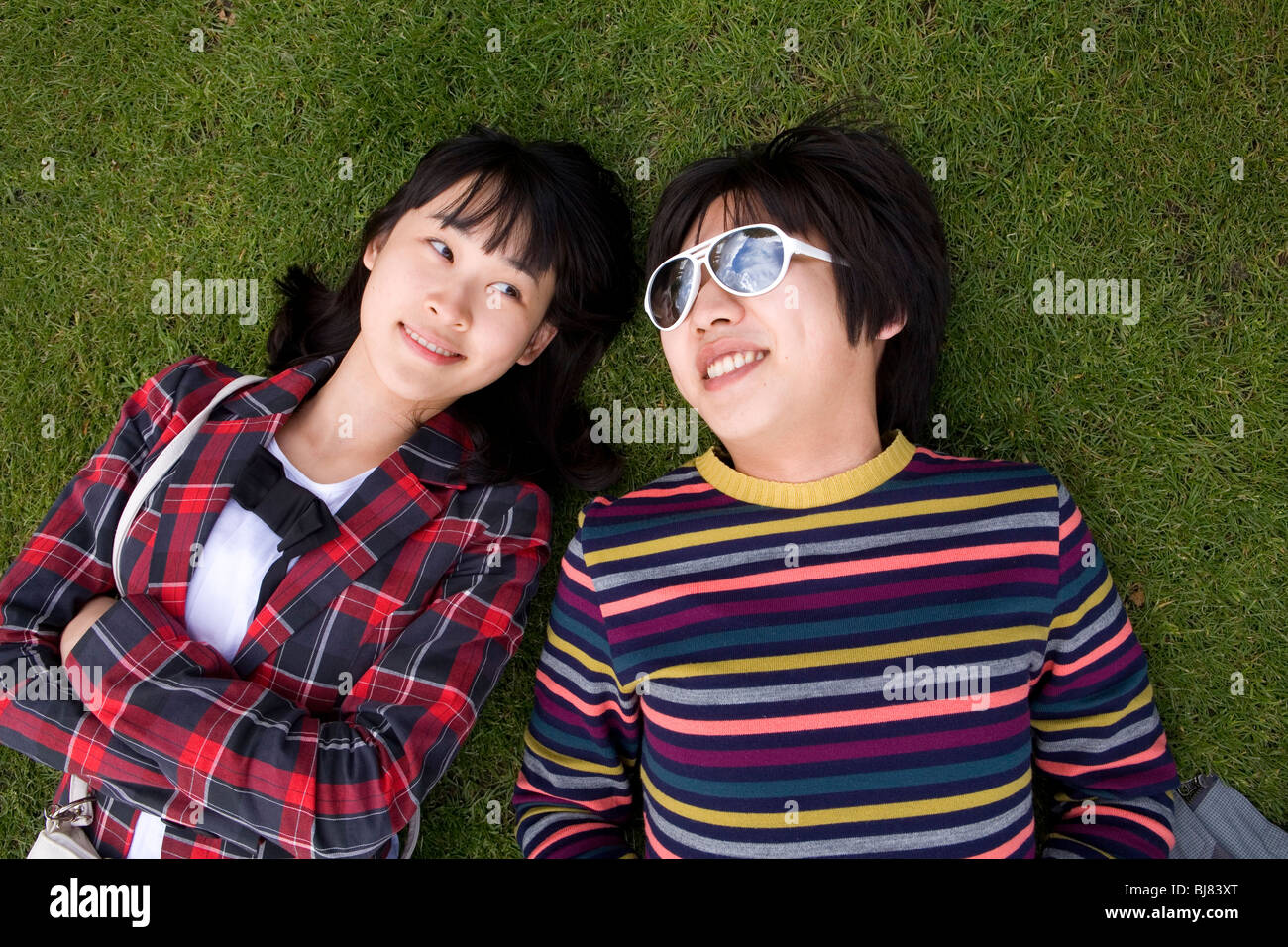 Young asian couple lying on the grass in colourful clothes Stock Photo