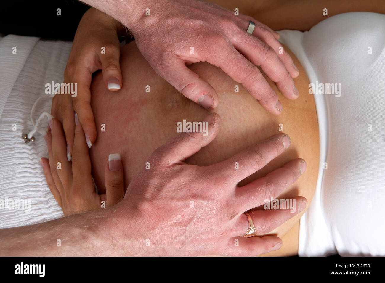 8 month pregnant 30 year old woman with 37 year old male partner hands on the bump Stock Photo