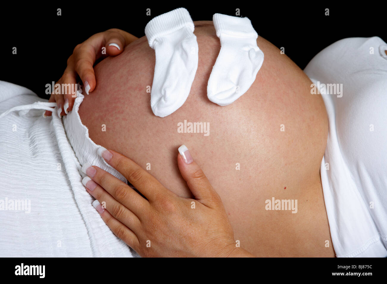8 month pregnant woman 30 years of age with baby bump and small baby socks Stock Photo