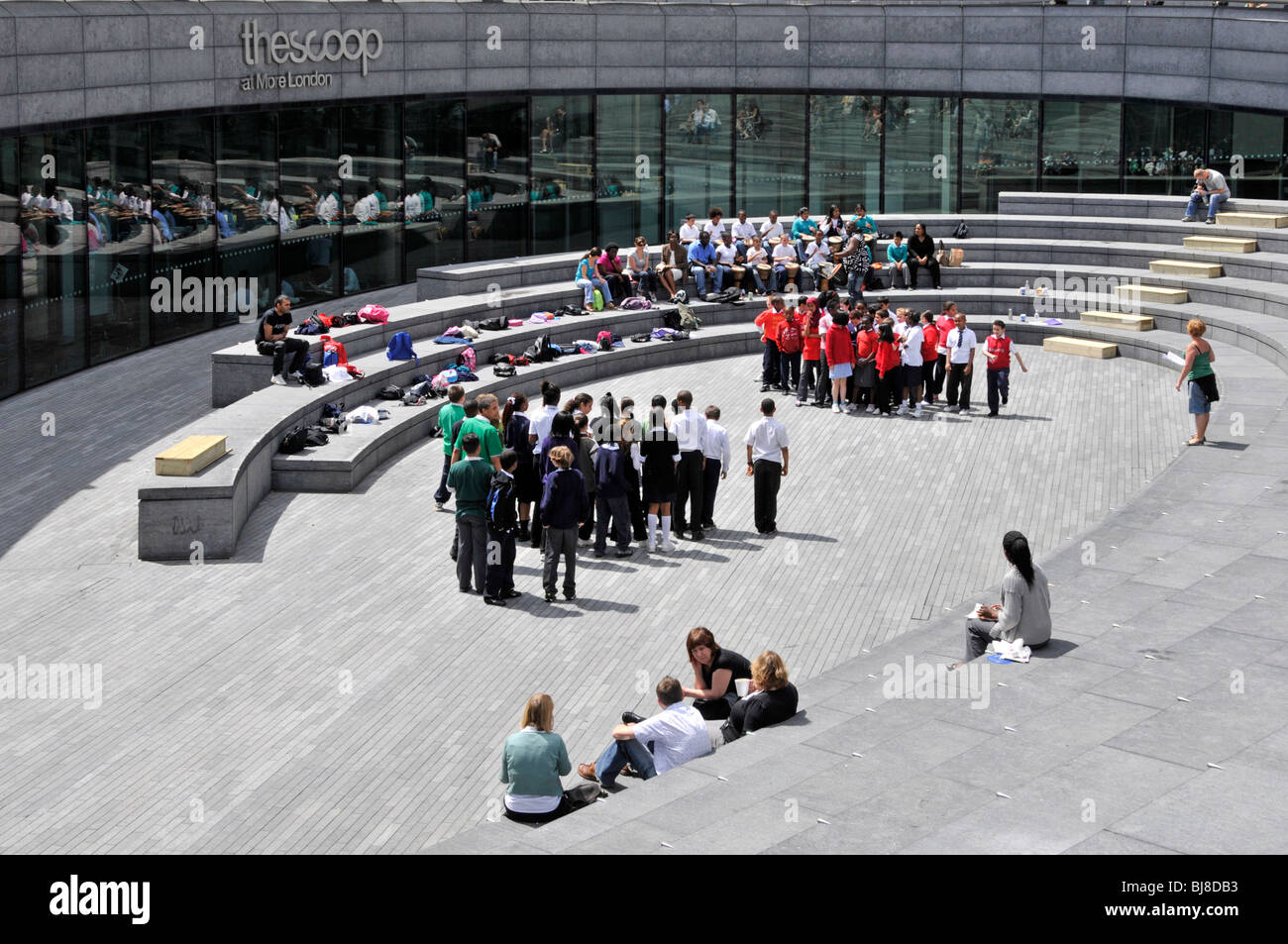 Group of school education trip children in sunshine in the Scoop amphitheatre amphitheater entertainment venue at More London Southwark England UK Stock Photo