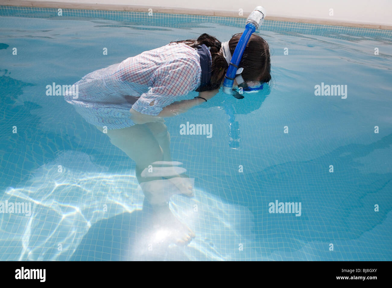 girl with clothes and snorkel studying bottom of swimming pool Stock Photo