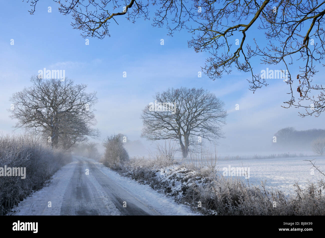 Winter snow covering farmland landscape foggy weather clearing to leave blue sky above country lane in rural Brentwood Essex countryside England UK Stock Photo