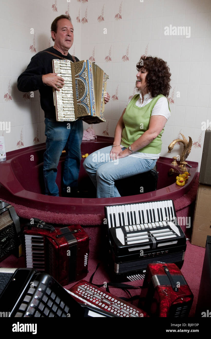 Man and woman singing and playing the accordion in a corner bathtub surrounded by accordions Stock Photo