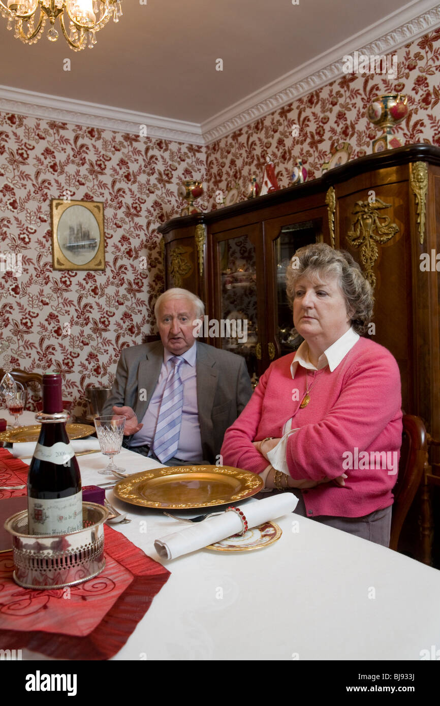 senior couple arguing with someone outside frame while seated by a set table in diningroom with outrageous decor and wallpaper Stock Photo