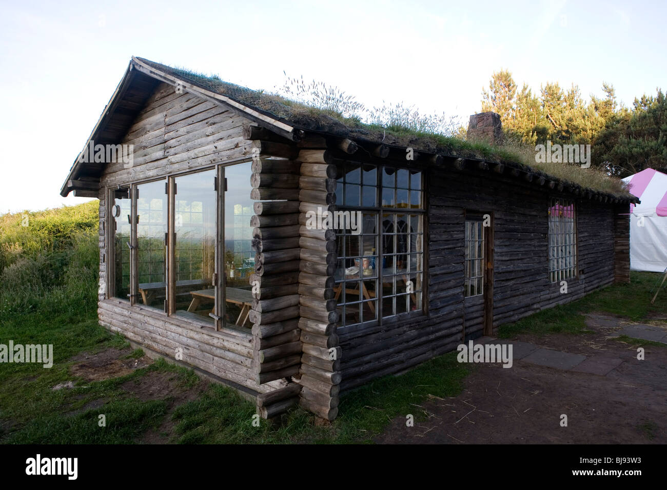 wooden country cottage with turfed roof and large windows, party tent in the background Stock Photo