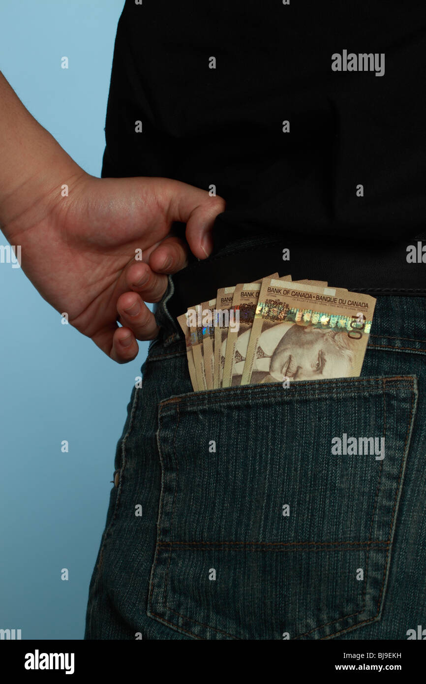 A man standing with his hand on his hip and a fan of Canadian one hundred dollar bills sticking out of his back pocket. Stock Photo