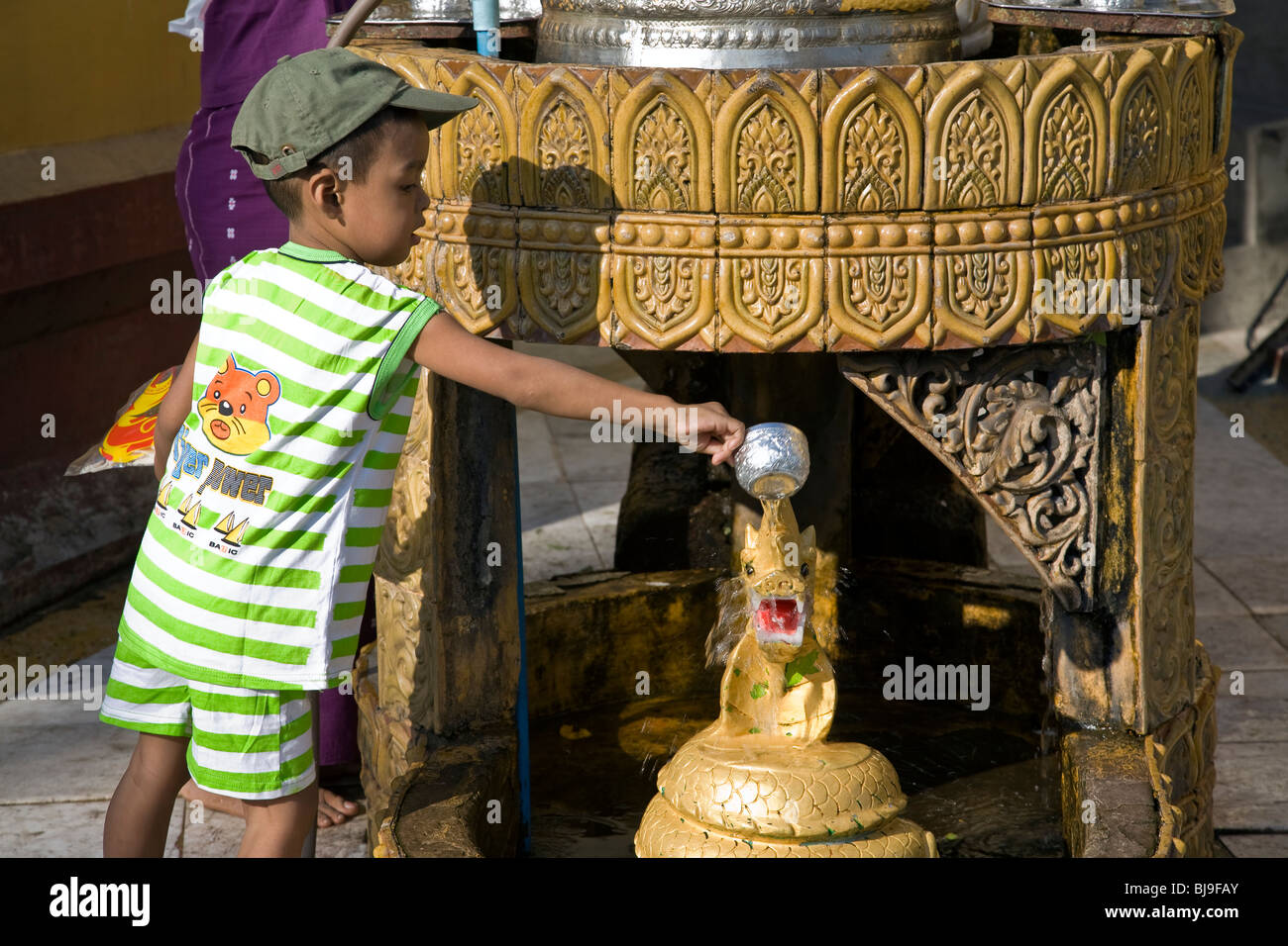 Burmese boy pouring water over a dragon statue (buddhist ritual