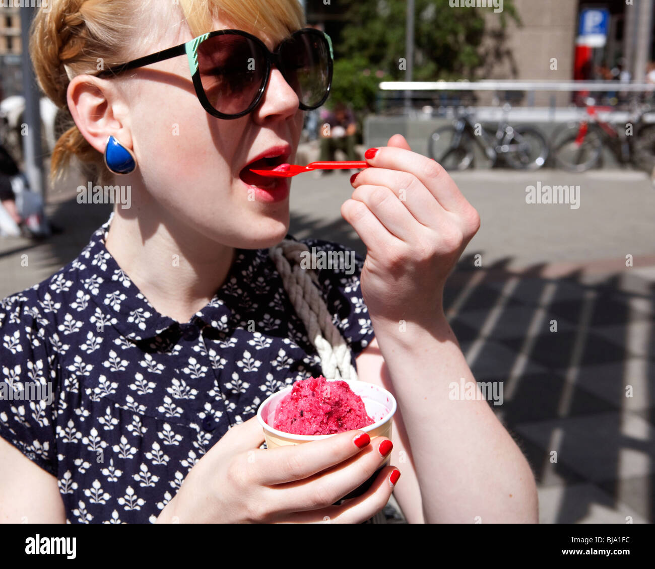 blonde girl in funky sunnglasses eating pink ice cream on the street Stock Photo