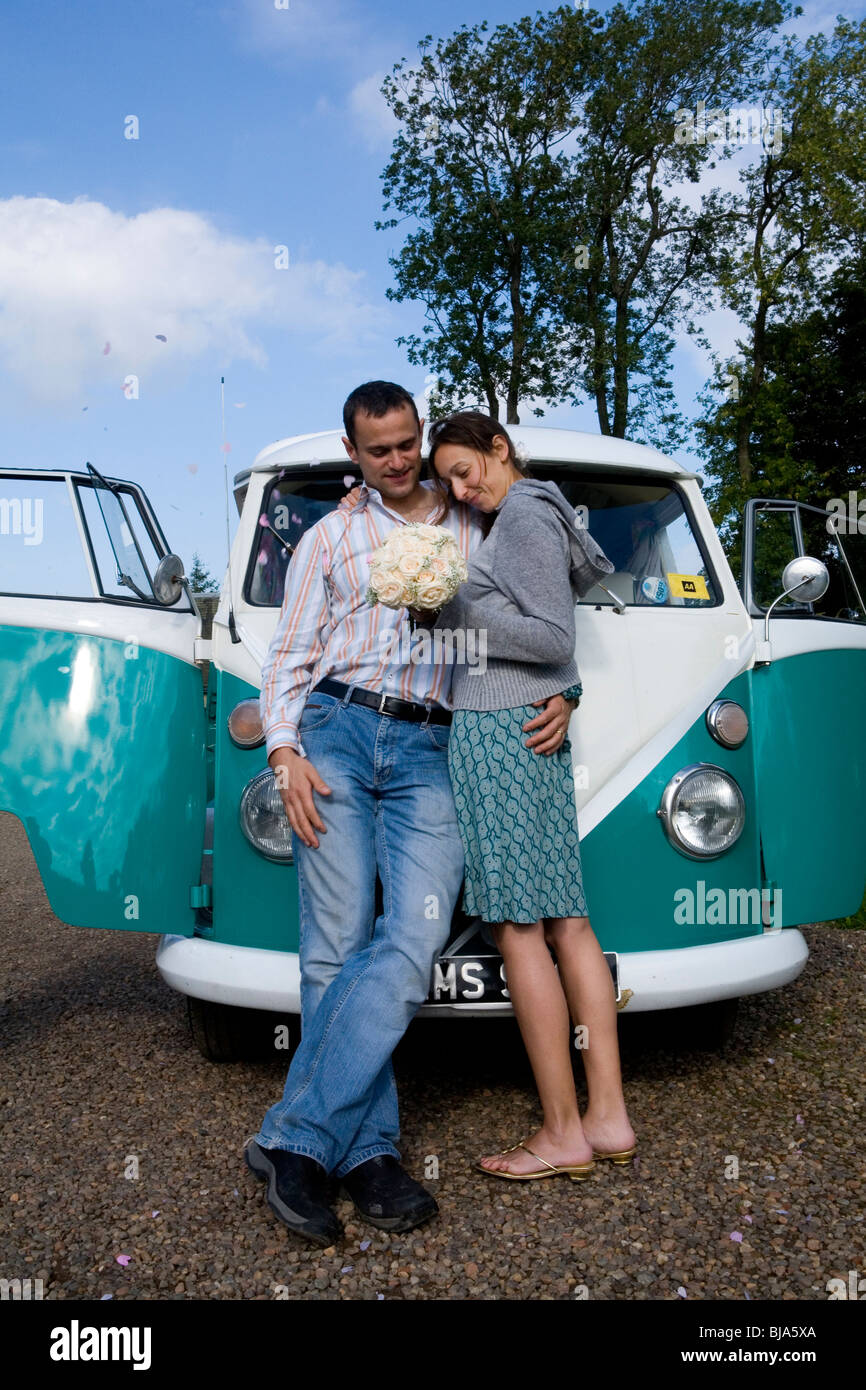 newly weds posing infront of their turquoise vw campervan before going on honeymoon Stock Photo