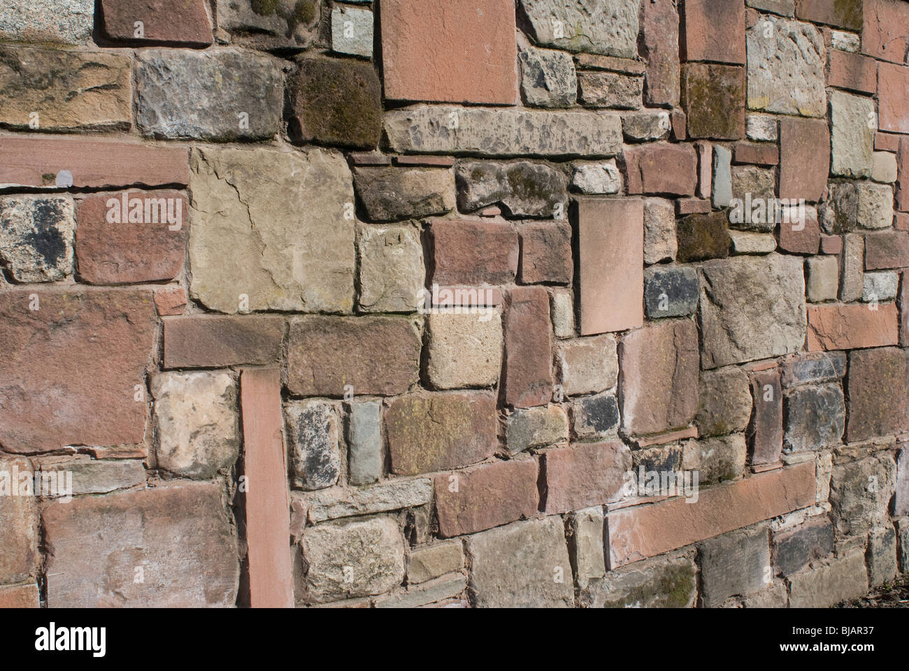 A solid stone wall made of sandstone limestone and granite. Stock Photo