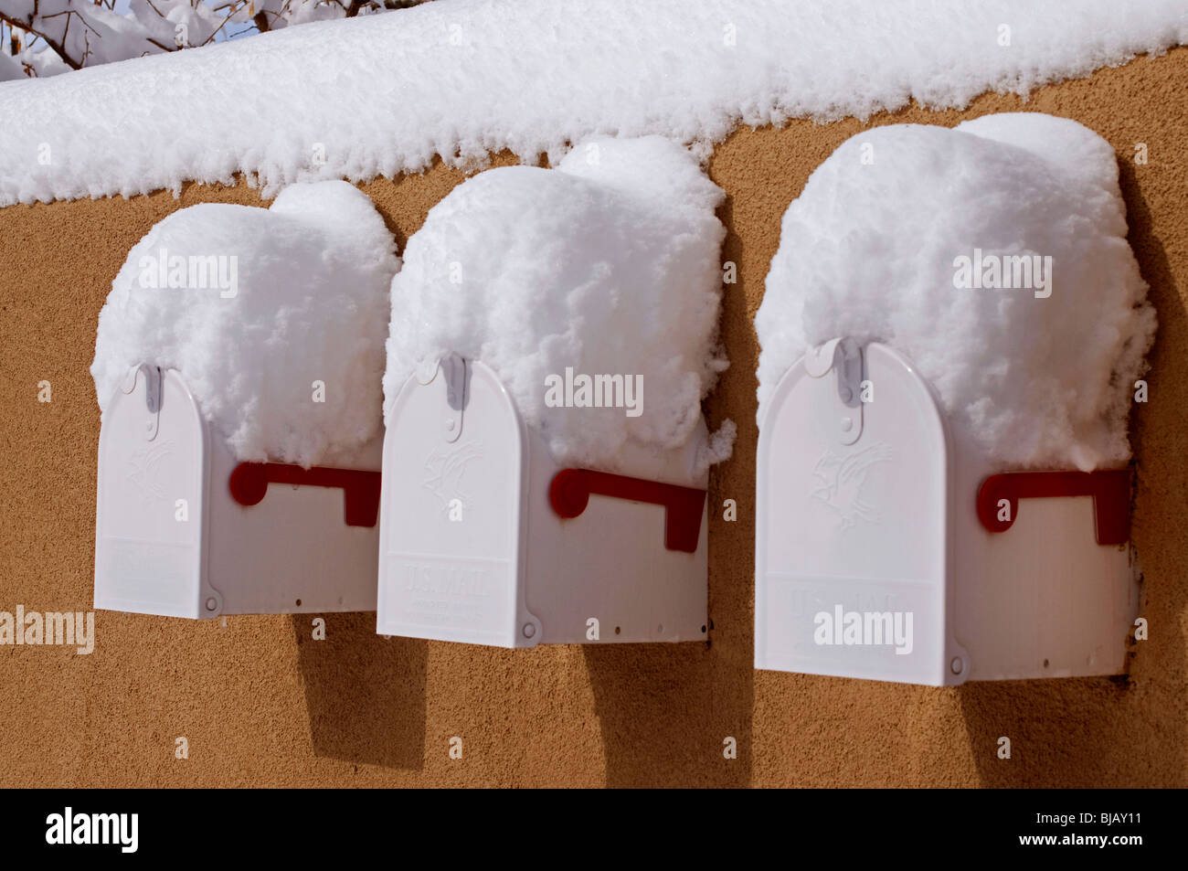 Three white mailboxes built into adobe wall covered with snow. Stock Photo