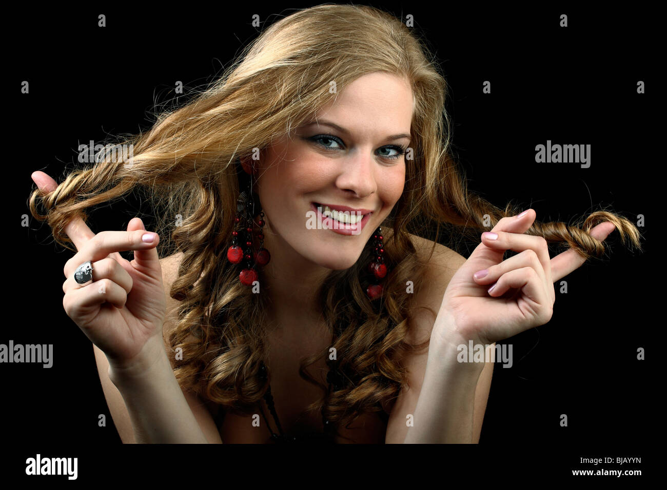 Beautiful girl wrapping her curly hair around both index fingers isolated on black Stock Photo