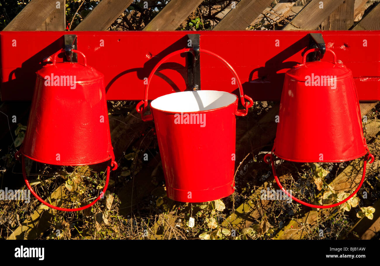 Bright red painted fire buckets hanging on a wooden fence Stock Photo