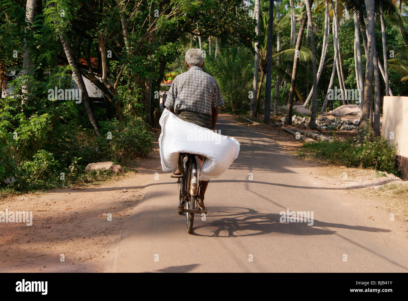A Old aged Poor native Indian village Farmer Carrying Heavy weight bag in his old cycle through the Village road Stock Photo