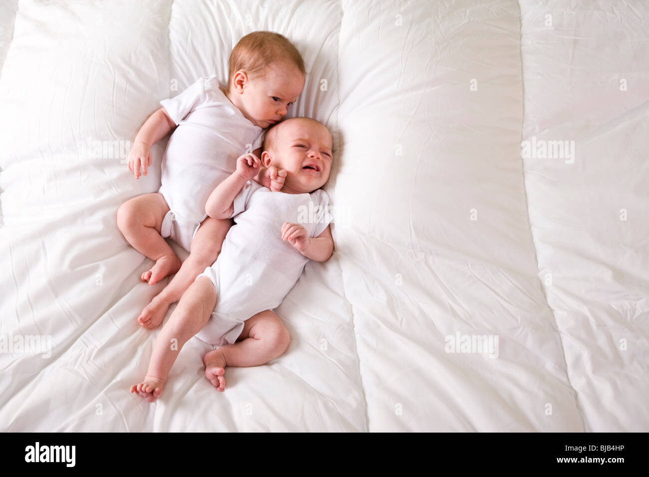 Newborn twin babies lying side by side on soft white blanket, one