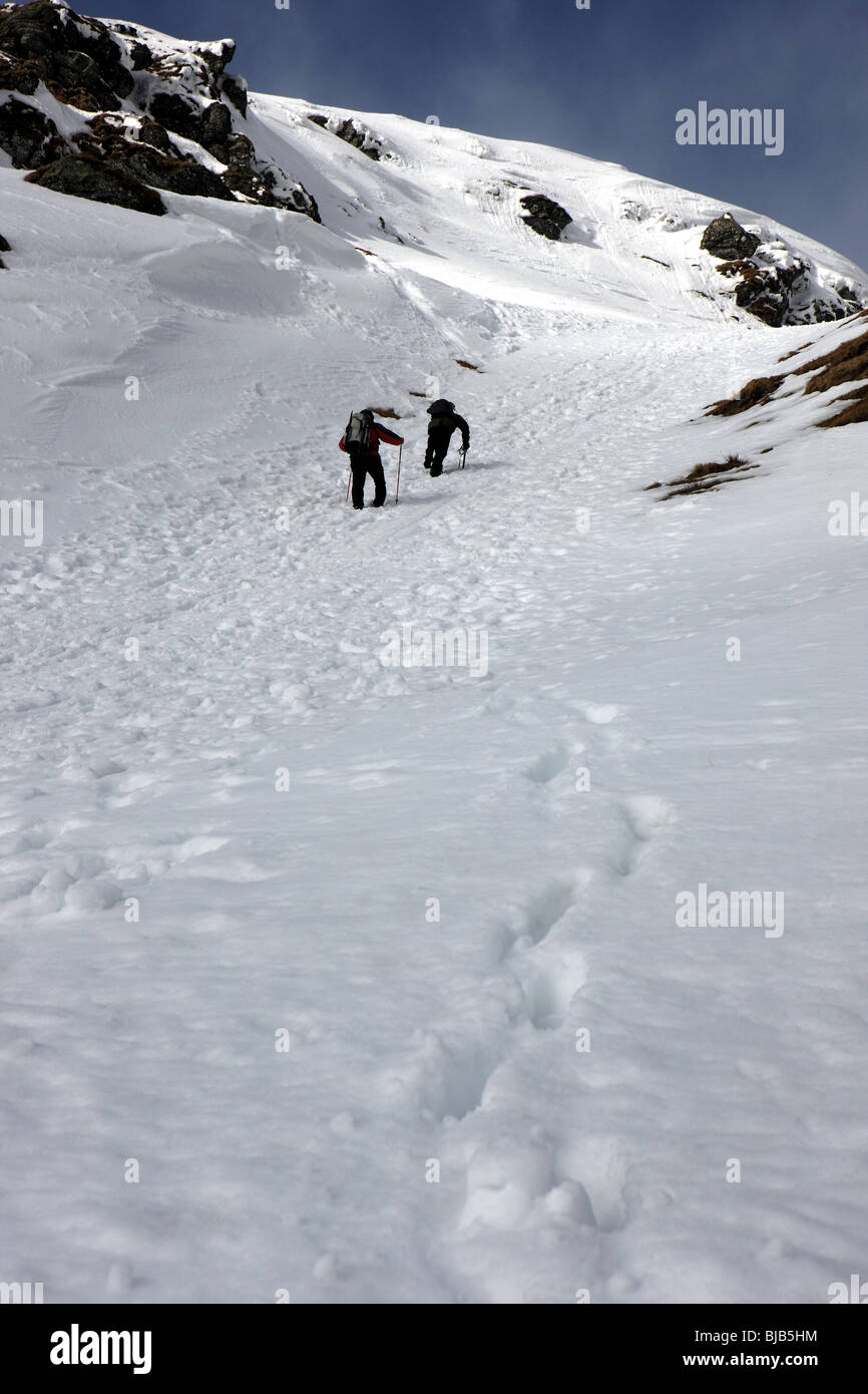 Two walkers climbing the snowy crags of Cam Chreag  towards the summit of Meall Nan Tarmachan Stock Photo