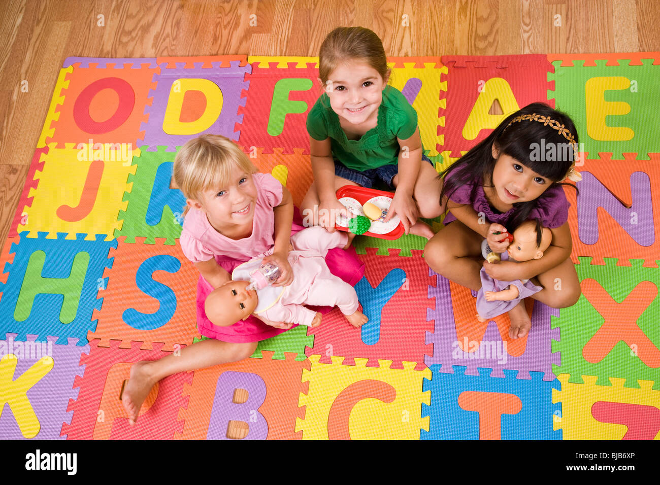 Little preschool girls playing with dolls on colorful alphabet mat Stock Photo