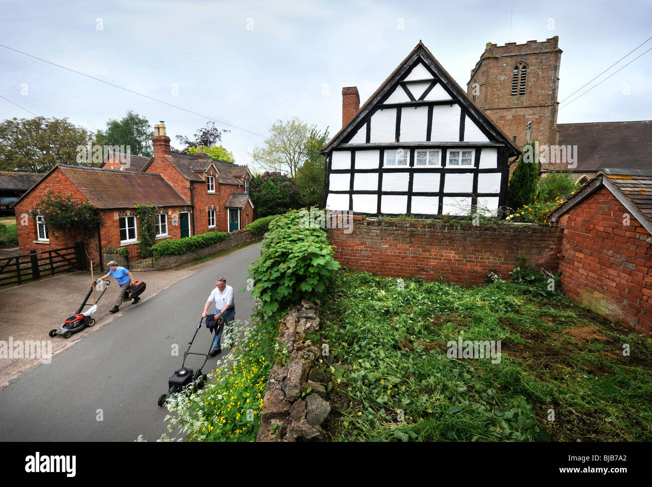 Gardeners push lawnmowers through the village of Redmarley D'Abitot, Gloucestershire with the Church of St Bartholomew's Stock Photo