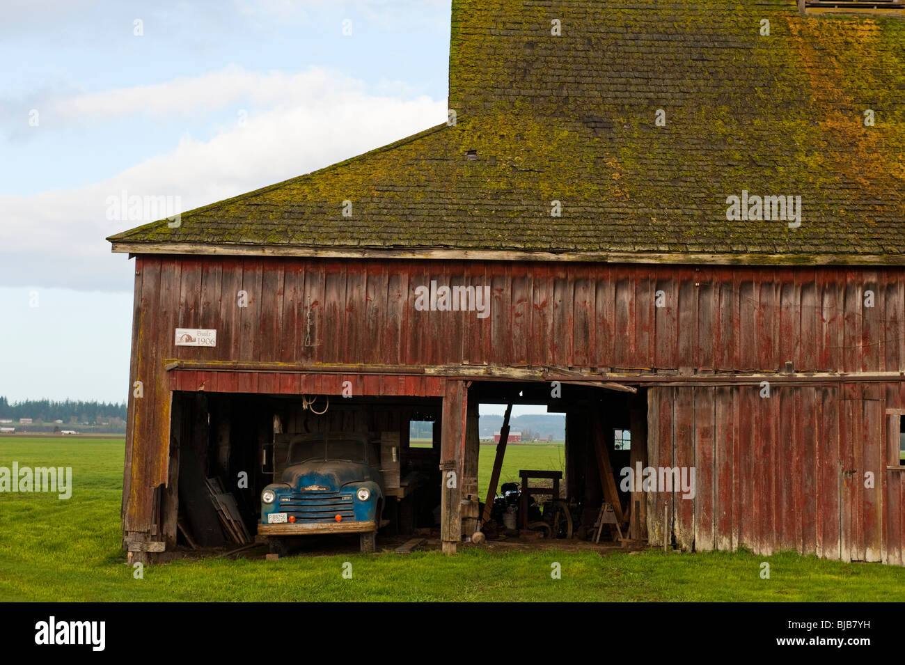 An old barn with a vintage truck parked under the sloping roof located in the Skagit Valley of northwest Washington State. Stock Photo
