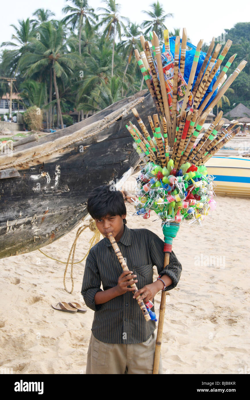 A Poor Flute Seller Boy playing his Flute in the Hard Noon time at Kovalam Beach Shore.A Typical Child Labor Scene from India Stock Photo