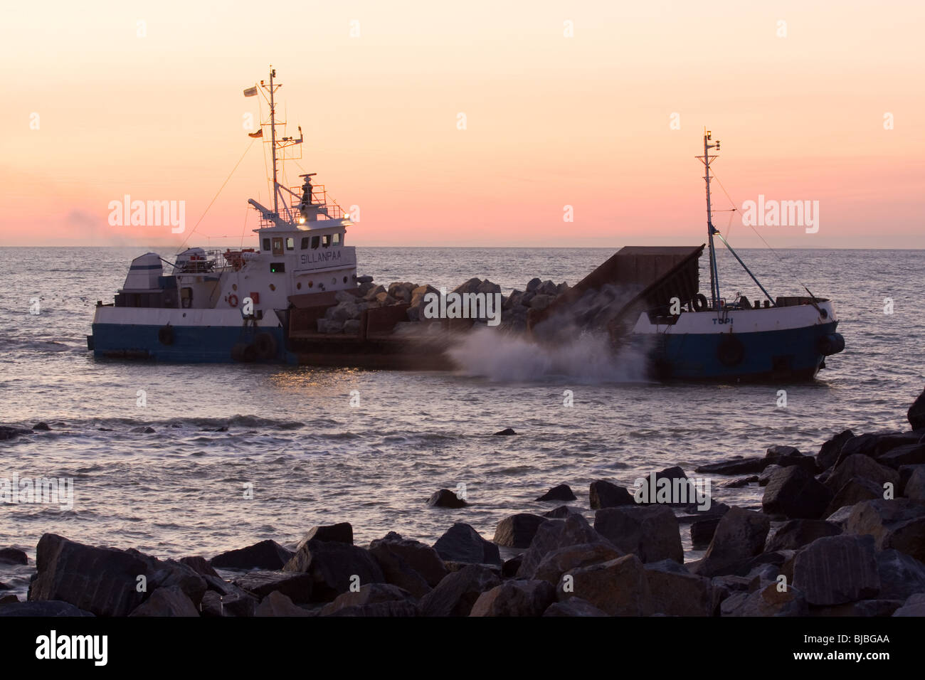 Boat delivering rocks for sea defence. Stock Photo