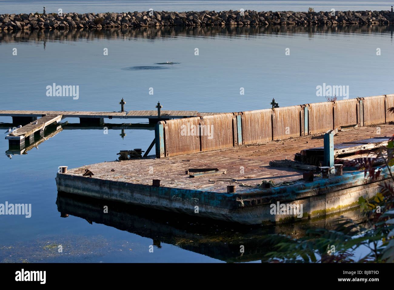 An old dilapidated marina platform, surrounded by still water, with a break wall in the background. Lake Ontario, Canada Stock Photo