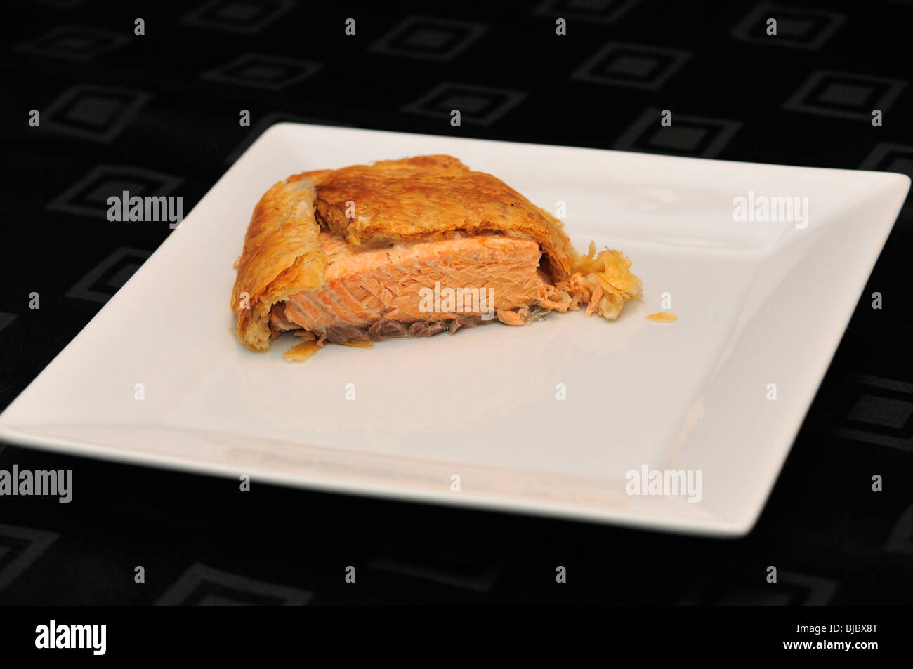 Salmon en croute on white serving plate on black table cloth Stock