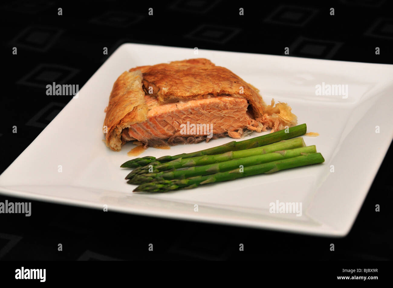 Salmon en croute with Green Asparagus on white serving plate on black table cloth Stock Photo