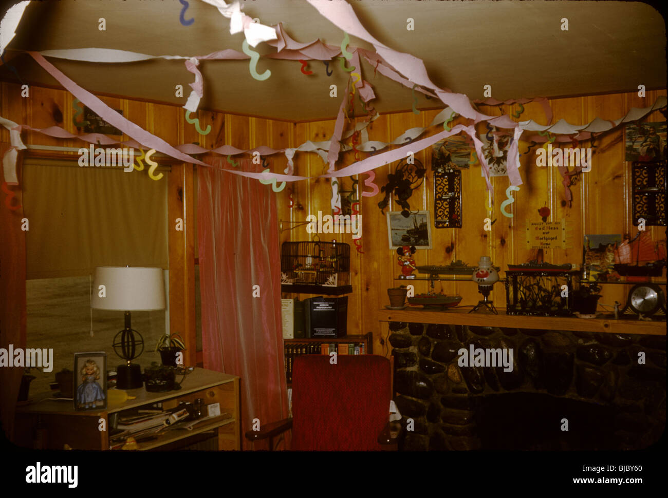 A room inside a house with wood panel walls is decorated for a New Years party during the late 1950s. celebration ribbons Stock Photo