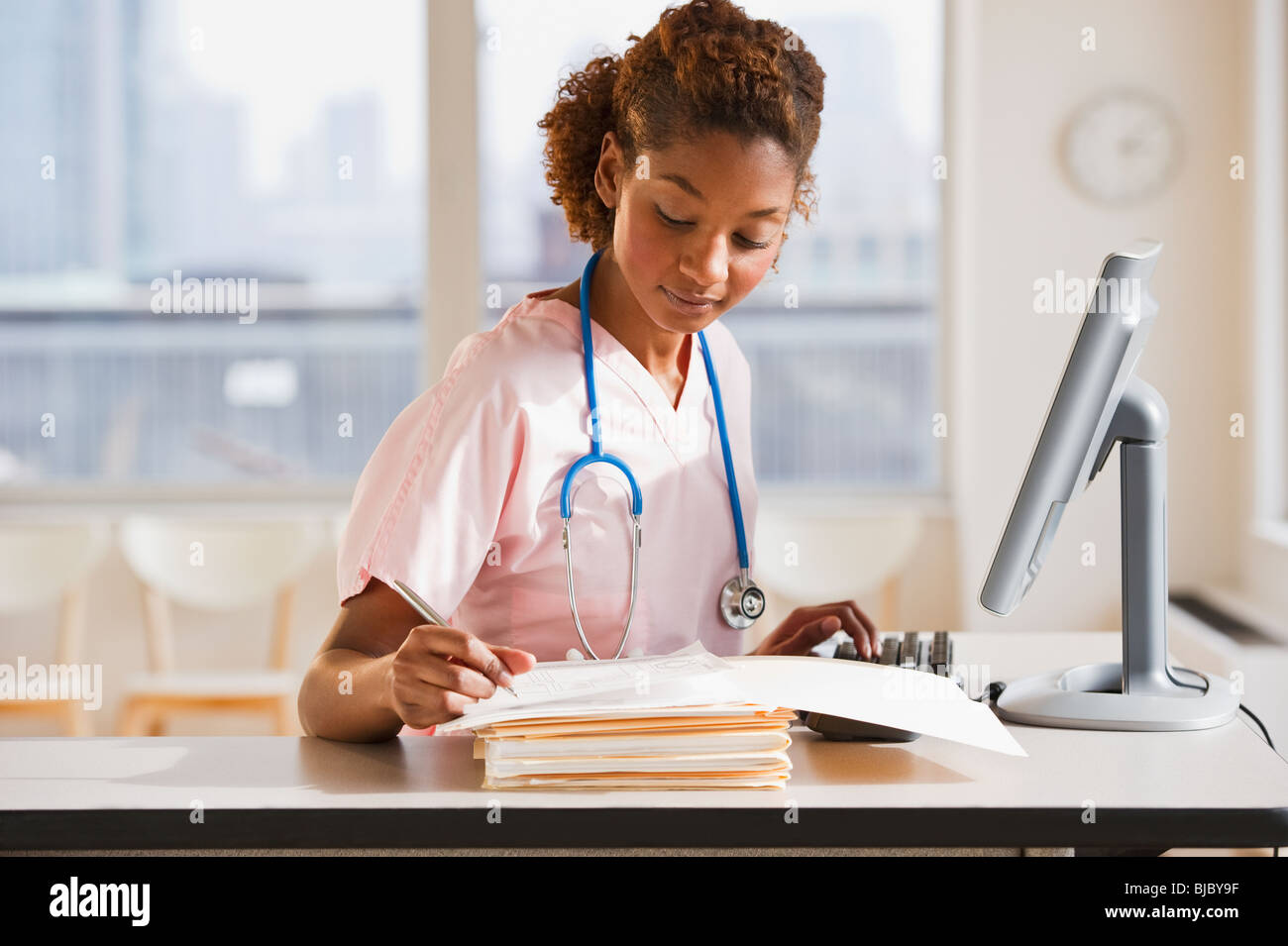 Mixed race nurse working on medical charts at computer Stock Photo