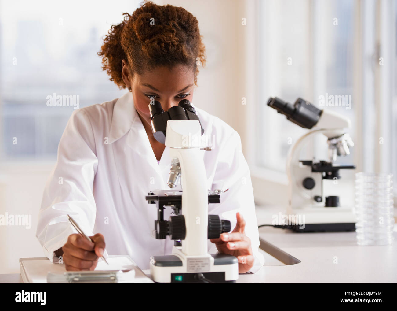Mixed race scientist peering into microscope Stock Photo