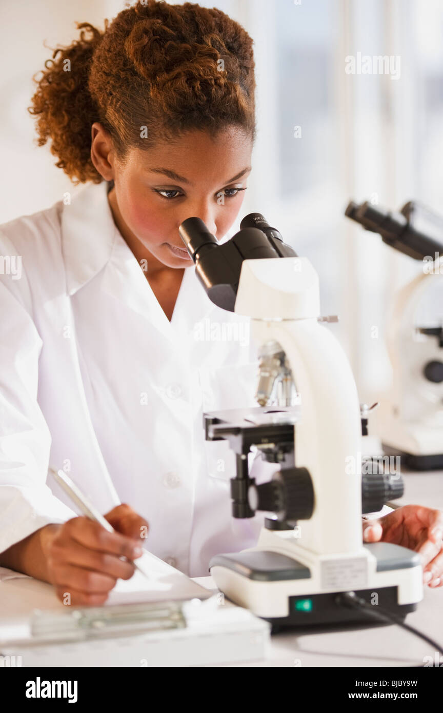 Mixed race scientist peering into microscope Stock Photo