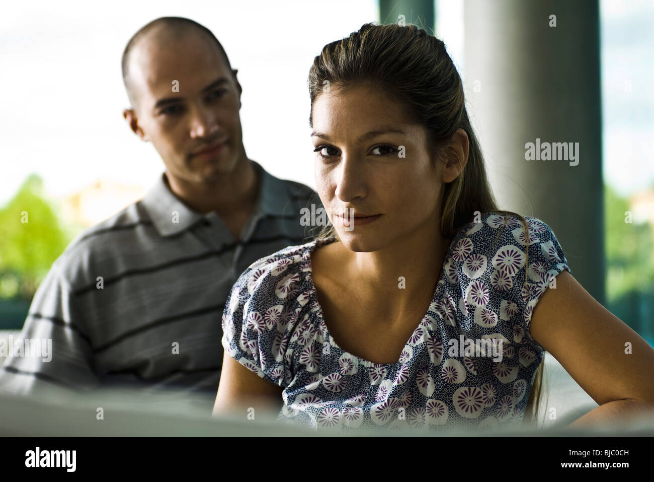 Young woman looking at camera, husband in background Stock Photo
