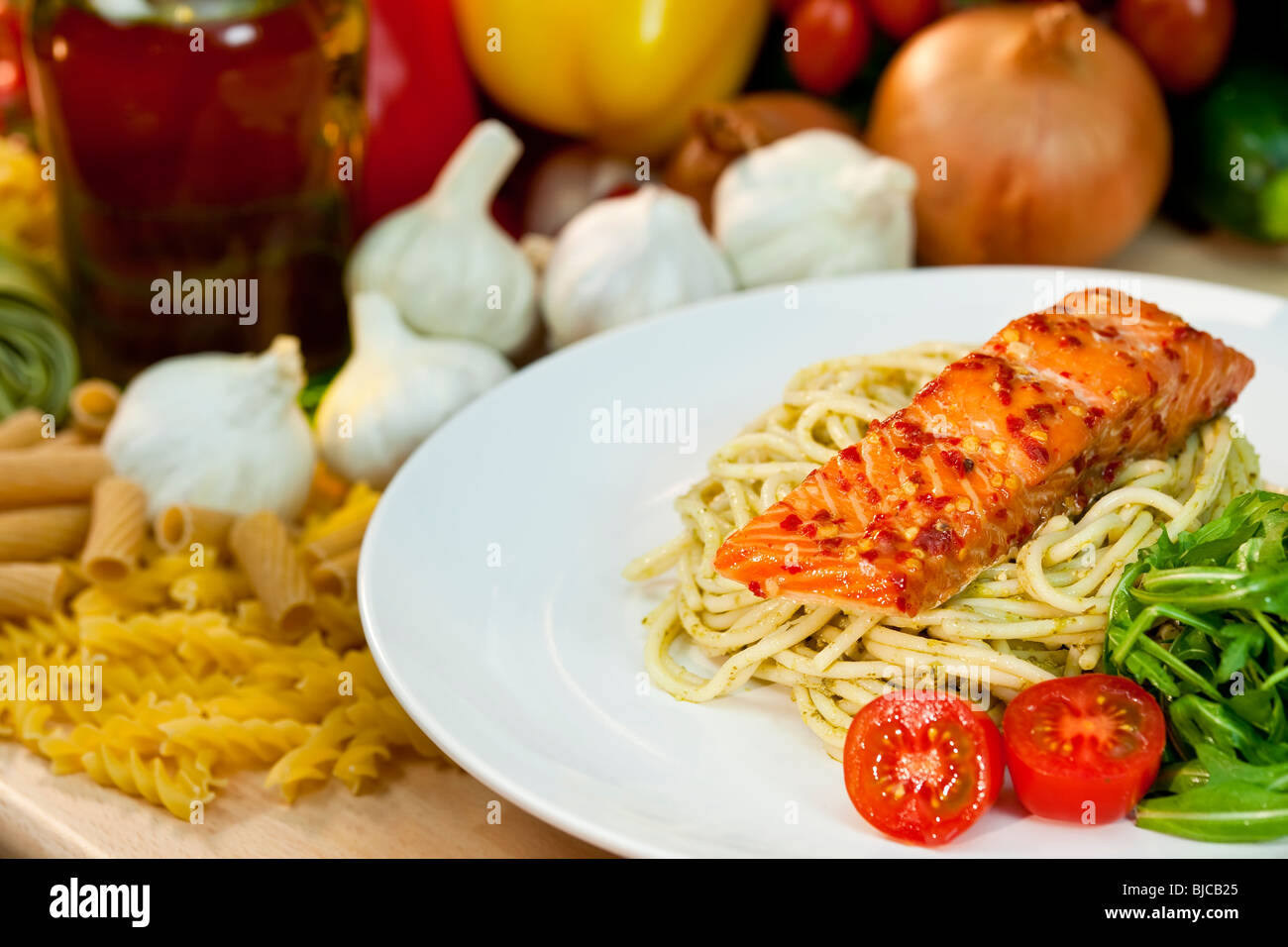 Seared chili salmon fillet with pesto spaghetti, rocket salad and cherry tomatoes with other ingredients in the background Stock Photo