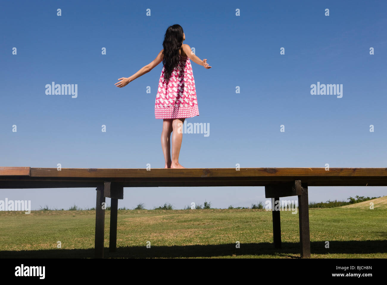 Woman standing on deck with arms out, rear view Stock Photo