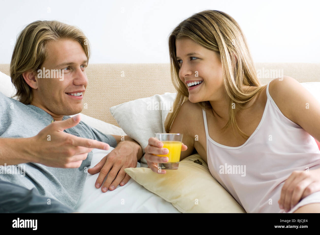 Couple talking together in bed, woman holding glass of orange juice Stock Photo