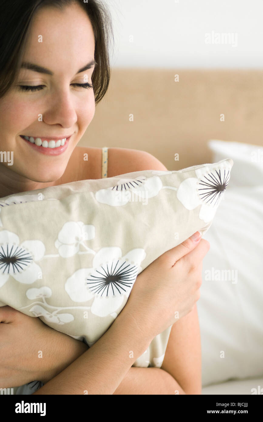 Young woman hugging pillow, smiling with eyes closed Stock Photo