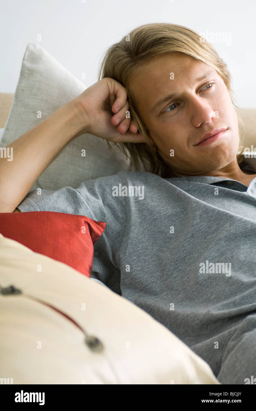 Man relaxing on pillows, looking away in thought Stock Photo