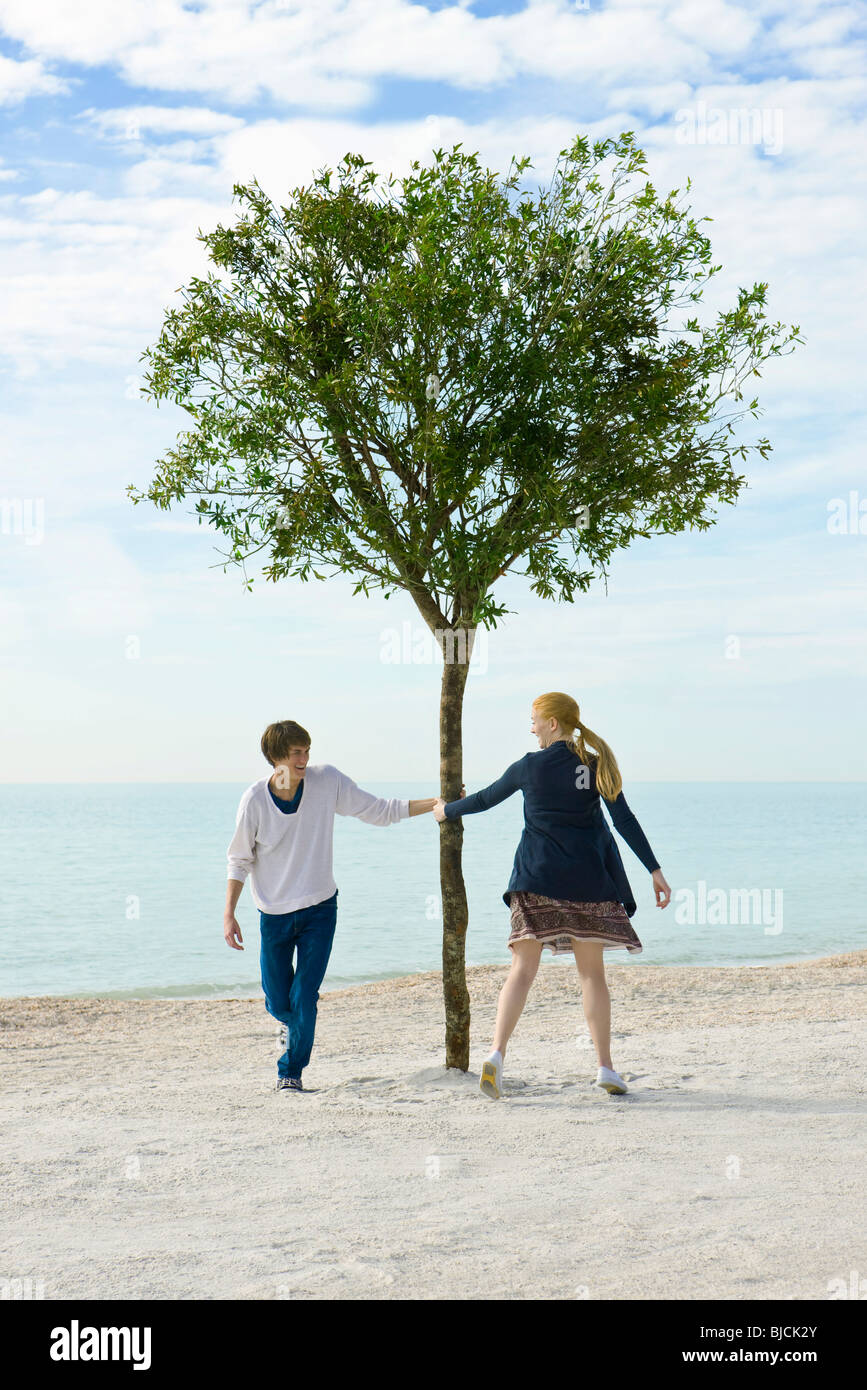 Young couple playfully pursuing one another around tree Stock Photo