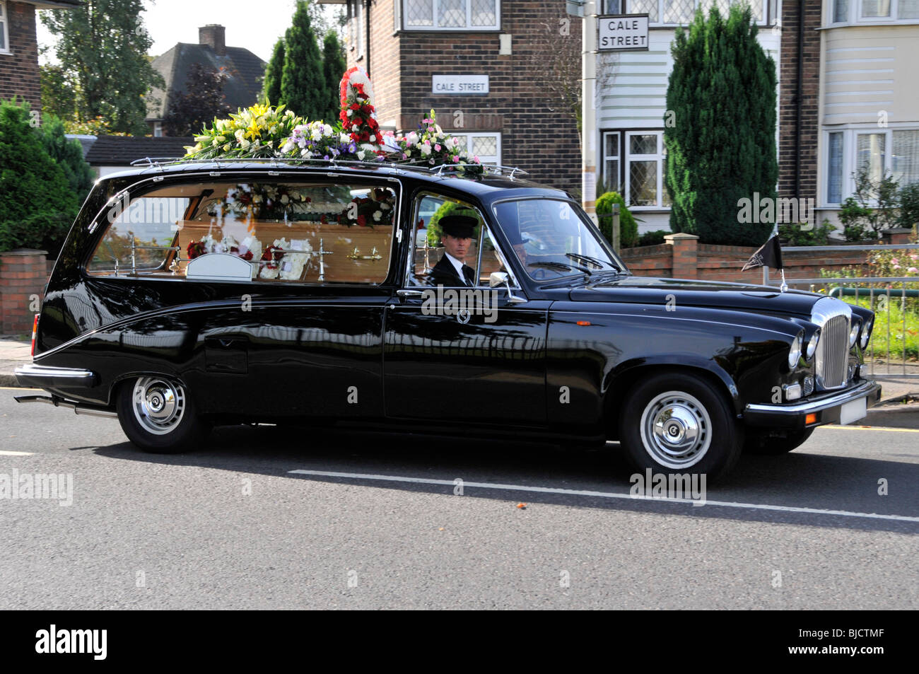 Funeral hearse car driving along residential street (street name and