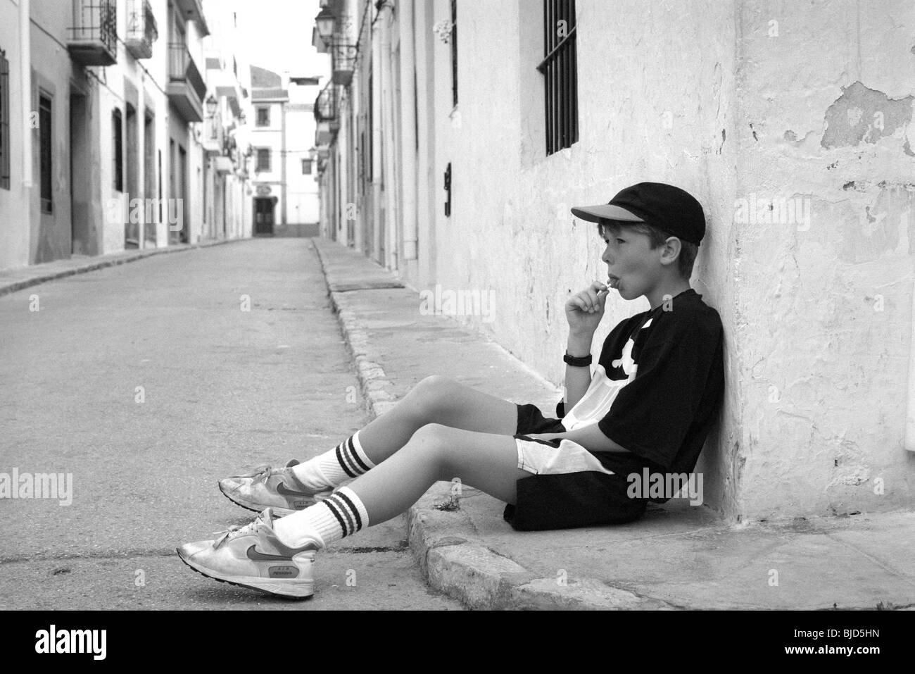 Young boy wearing baseball cap sucking lollipop in Javea Spain Stock Photo
