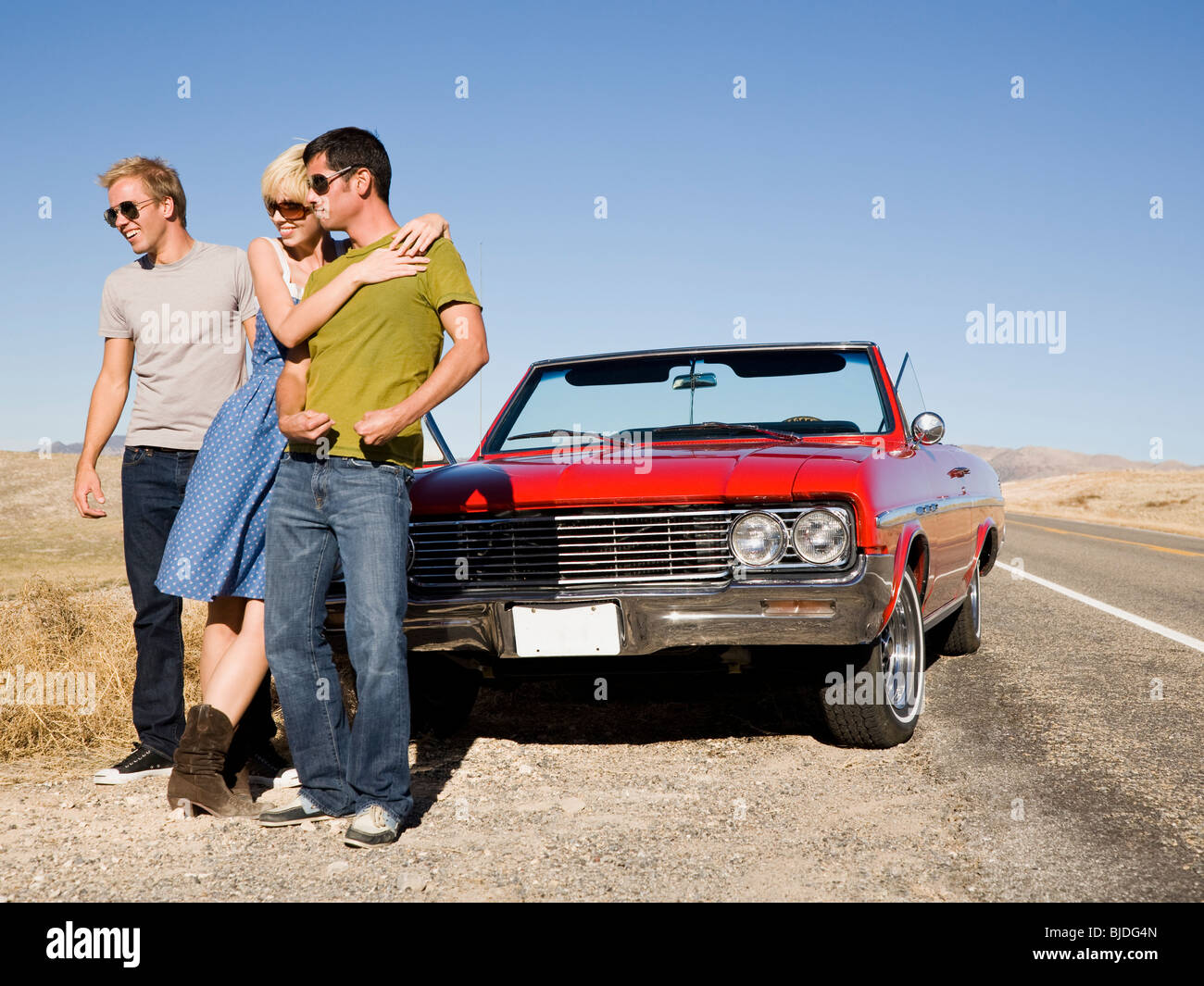 two men and a woman in front of a red convertible. Stock Photo