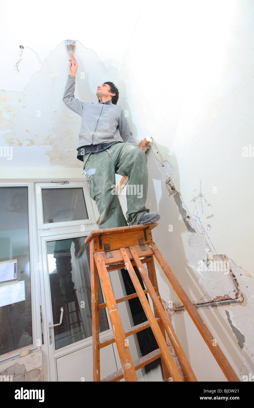 Man Working In Kitchen And Removing Old Paint Of Ceiling With